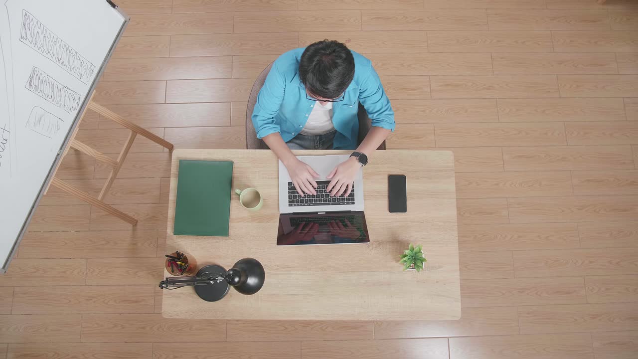 집에 있는 화이트보드 에 있는 나무 책상에 앉아 있는 스마트폰 에 노트북을 입력하는 남자의 상단 시각