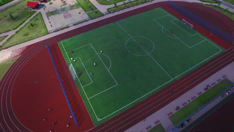 Aerial-view-soccer-players-playing-football-on-green-field-in-school-yard