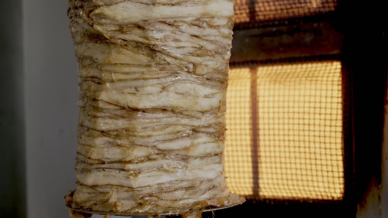 gran brocheta de shawarma de pollo colgada en la parrilla girando cerca del horno de gas