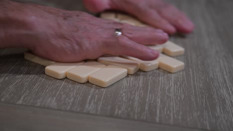 large rugged hands leap forward from a senior citizen mixing dominoes before the start of a game