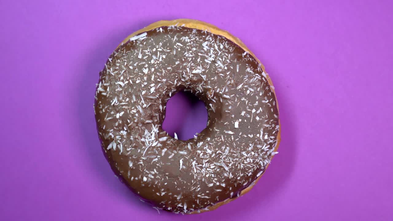 rosquilla de chocolate brillante y colorida con papas fritas de coco, tiro macro, girando sobre un fondo púrpura.