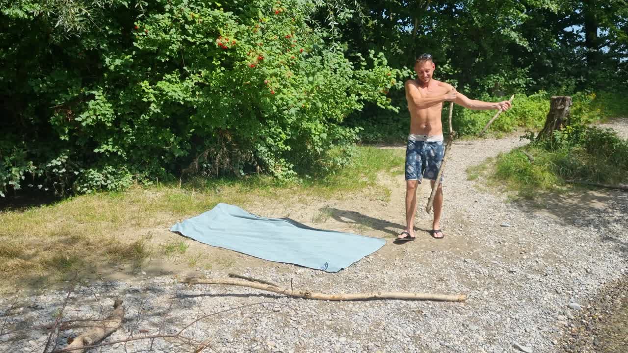 Attractive man in swimwear prepares firewood by hand for a riverside barbecue on the Aare near Bern on a hot, sunny Swiss summer day