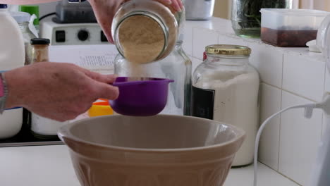 home baker measuring sugar and pouring it into a mixing bowl