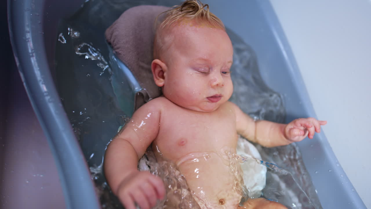 Blond infant child moving in the bath. Bathing time for the baby boy. Close up.