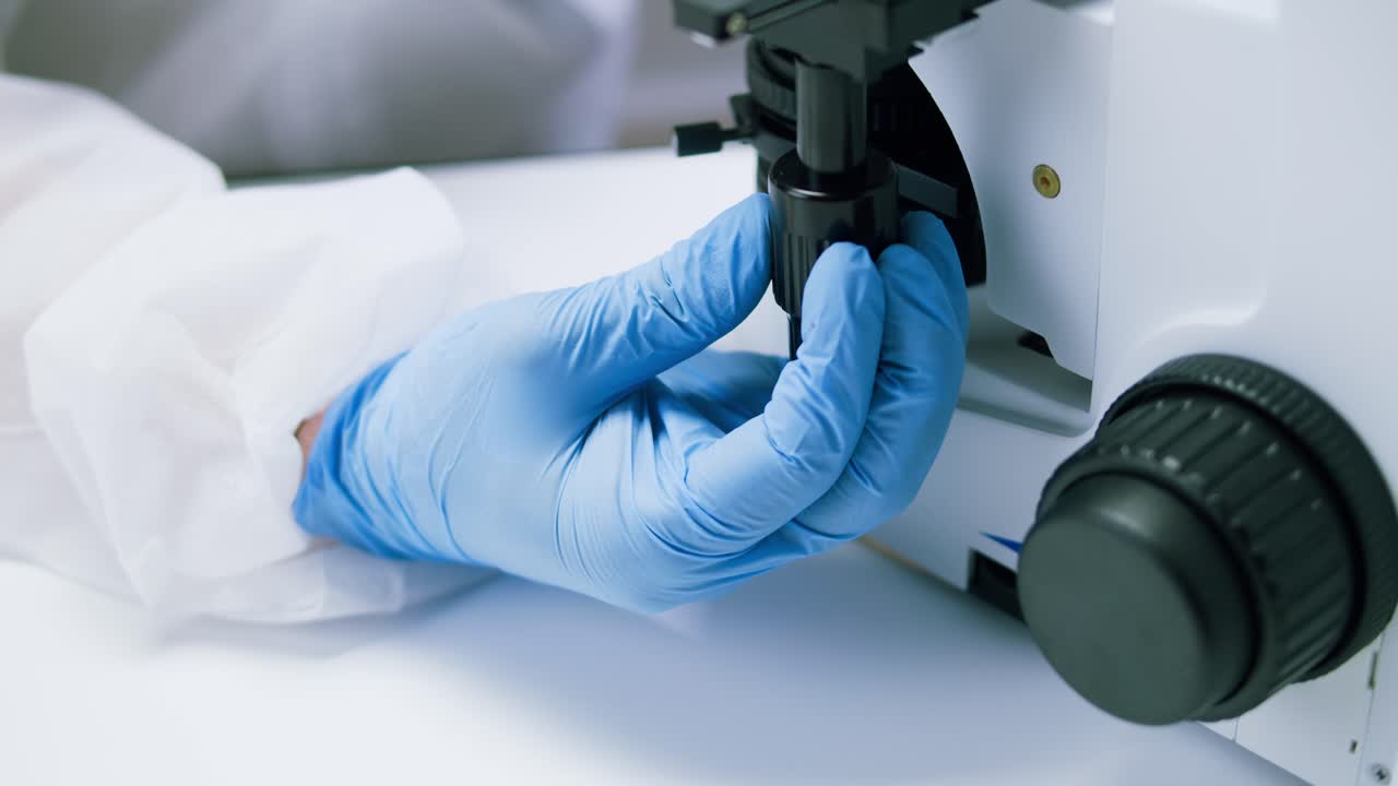 Gloved Hand Adjusting Microscope in a Laboratory Setting