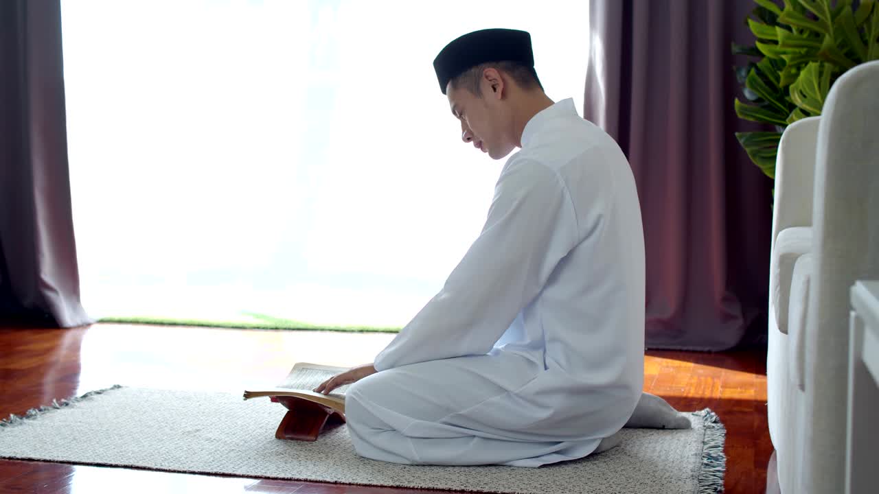 이슬람 의복 을 입은 젊은 이슬람 남자 가 꾸란 을 읽고 있다