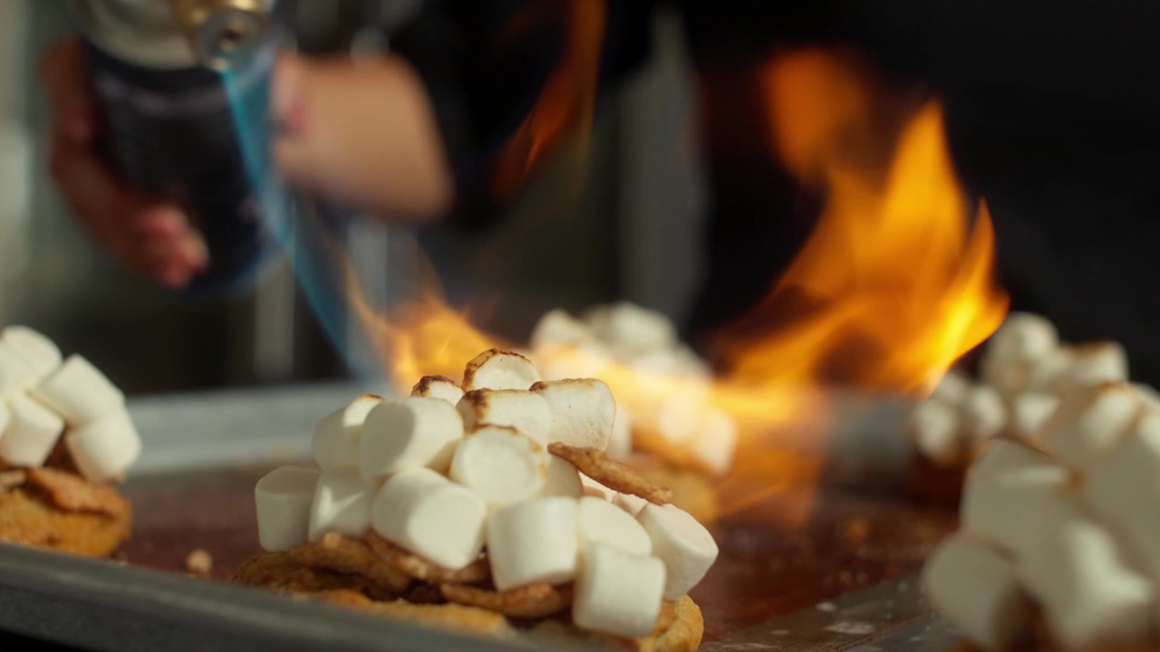 Cookies med skumfidus-topping ristes med en blå flammestråle fra en køkkenbrænder på en bageplade