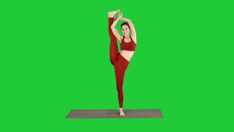 female yoga model making standing split smiling on a green screen, chroma key