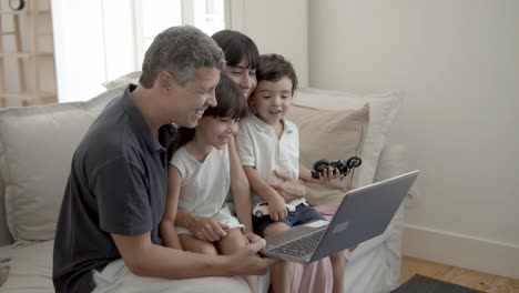 cheerful parents and two children with laptop in living room