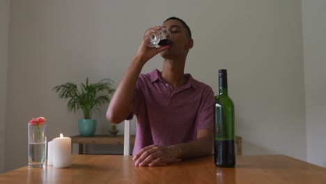 Smiling-mixed-race-man-sitting-at-table-with-lit-candle-drinking-red-wine-and-talking