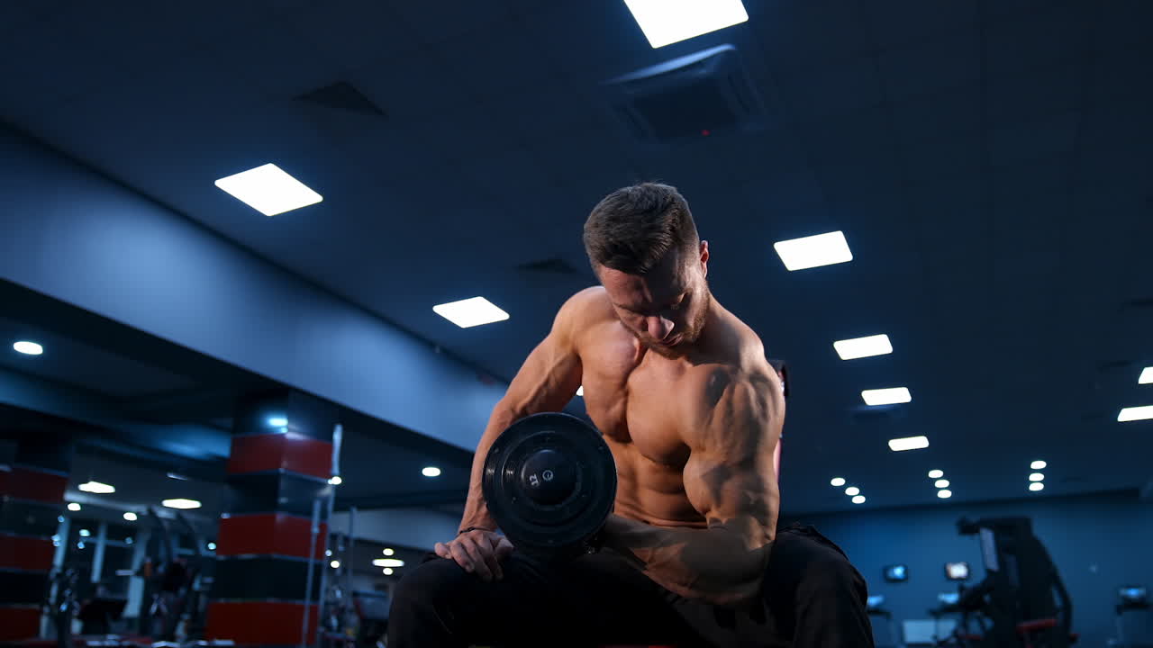 Fit muscular man exercising with dumbbell. Muscular young man lifting weights on gym background with blue light filter.