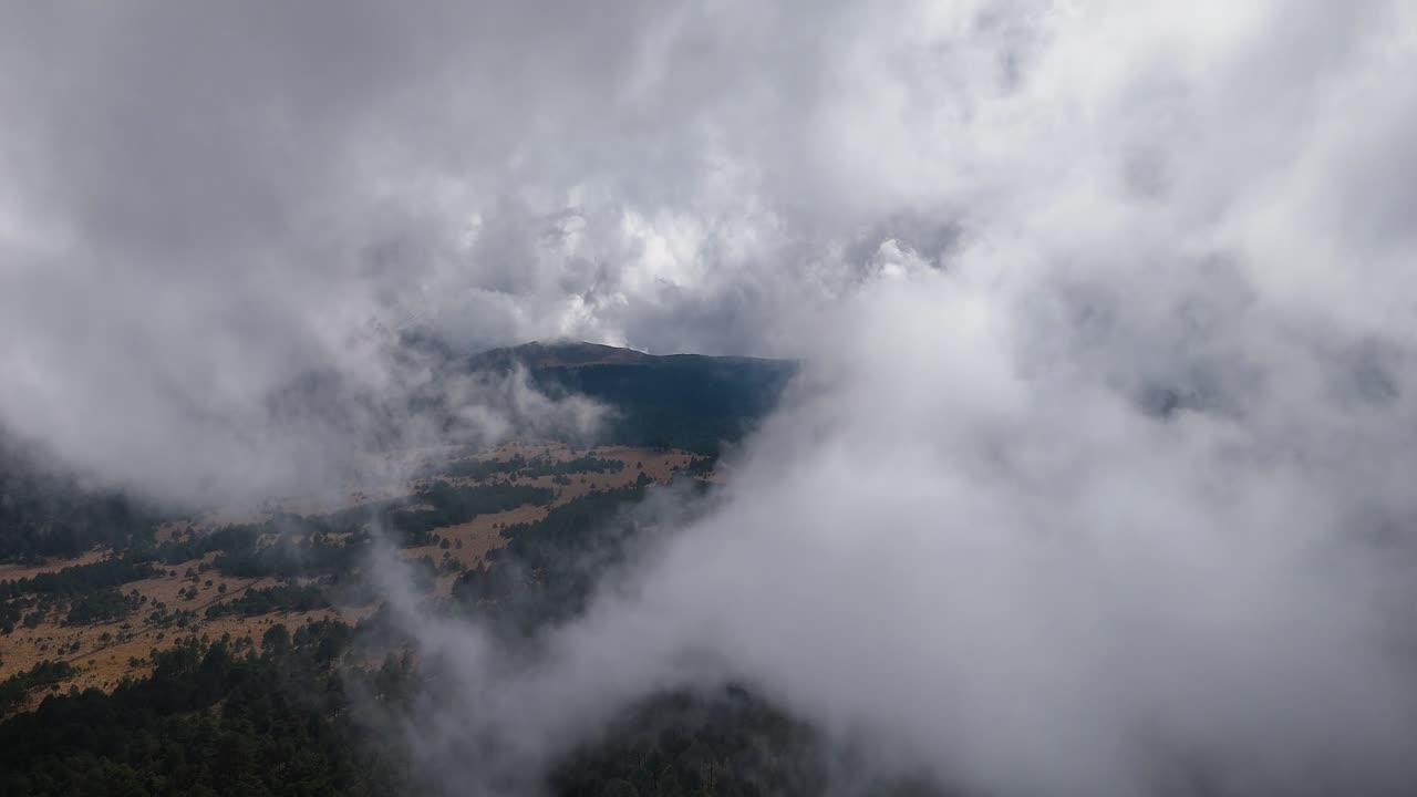 Ascending drone shot with clouds and mist covering the mountainous pass of Paso de Cortés in the metropolitan area of Mexico City