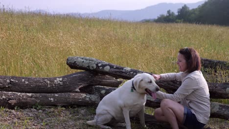 woman plays with white labrador retriever with mountain backdrop