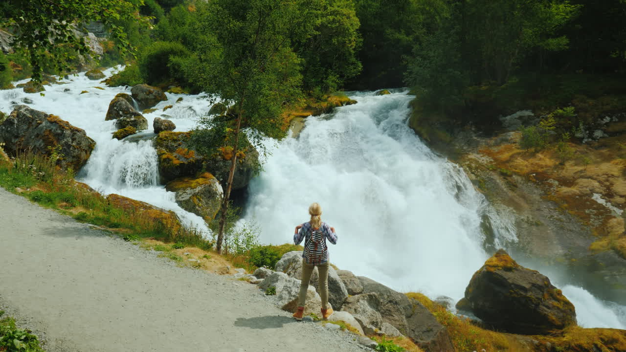 Resenären beundrar den stormiga bergsfloden som har sitt ursprung i Briksdalsglaciären. Den majestätiska scenen.