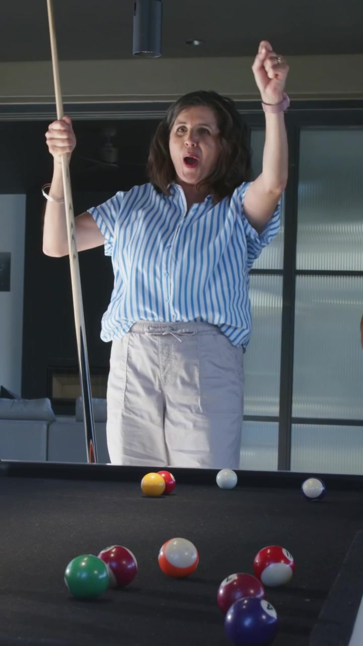 Vertical video: Reacting to shot woman in striped top pointing at pool table at home holding cue
