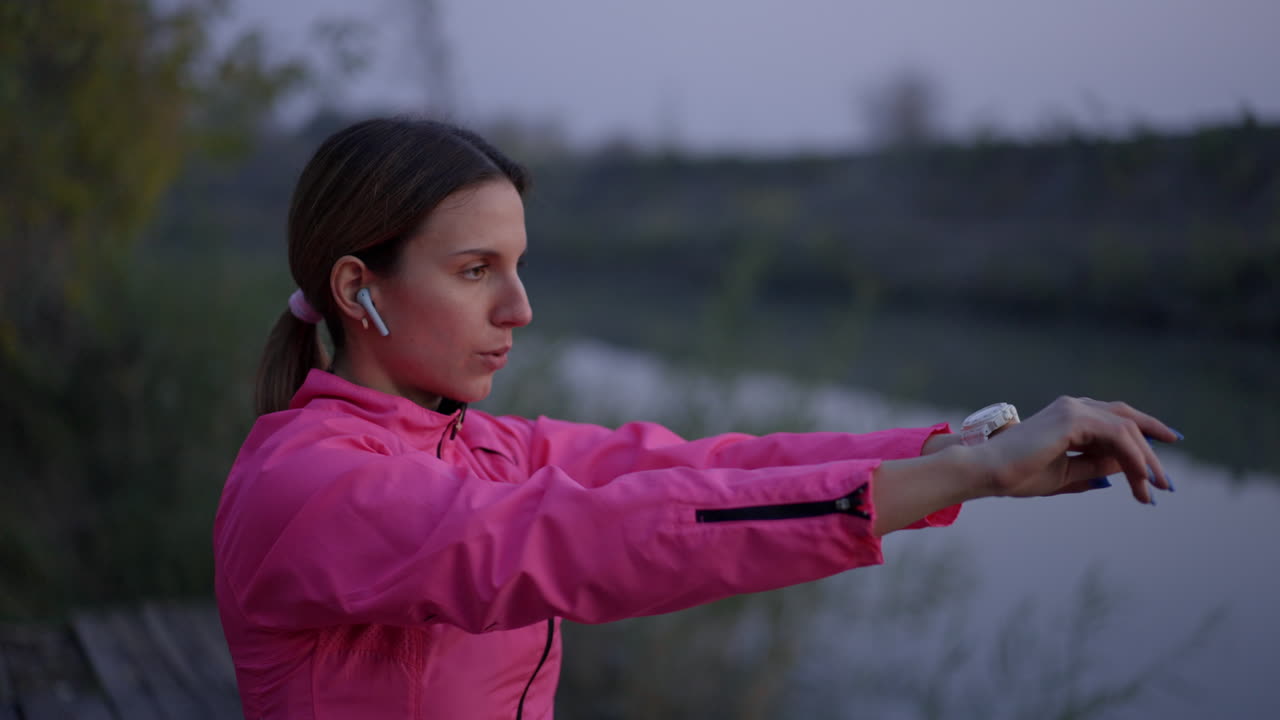 Woman Stretching Outdoors by Water in Pink Jacket