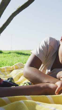 video of happy african american father and son having picnic on grass, arm wrestling