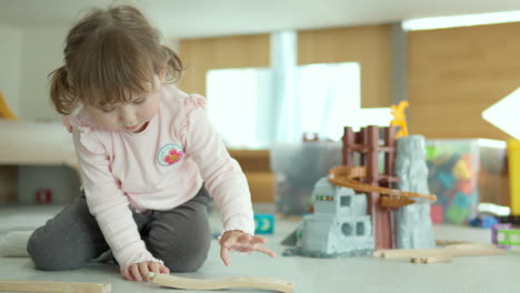 Lovely-Little-Child-Girl-Playing-Building-Wooden-Railroad-Track-on-a-Floor