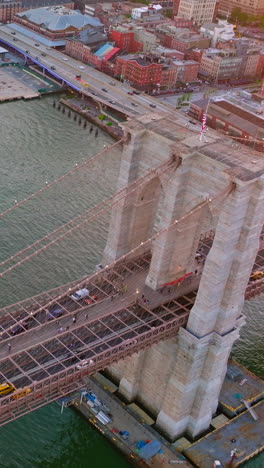 famous brooklyn bridge over east river in new york. numerous cars going along the bridge and yacht coming under it. aerial view. vertical video