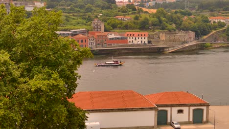 Traditional-Ferry-Boat-Cruising-In-The-Douro-River-Passing-By-The-Buildings-In-Porto,-Portugal