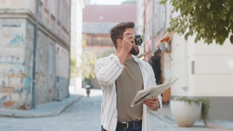 joven viajero turista feliz sosteniendo un mapa y tomando fotos usando una cámara retro en la calle de la ciudad