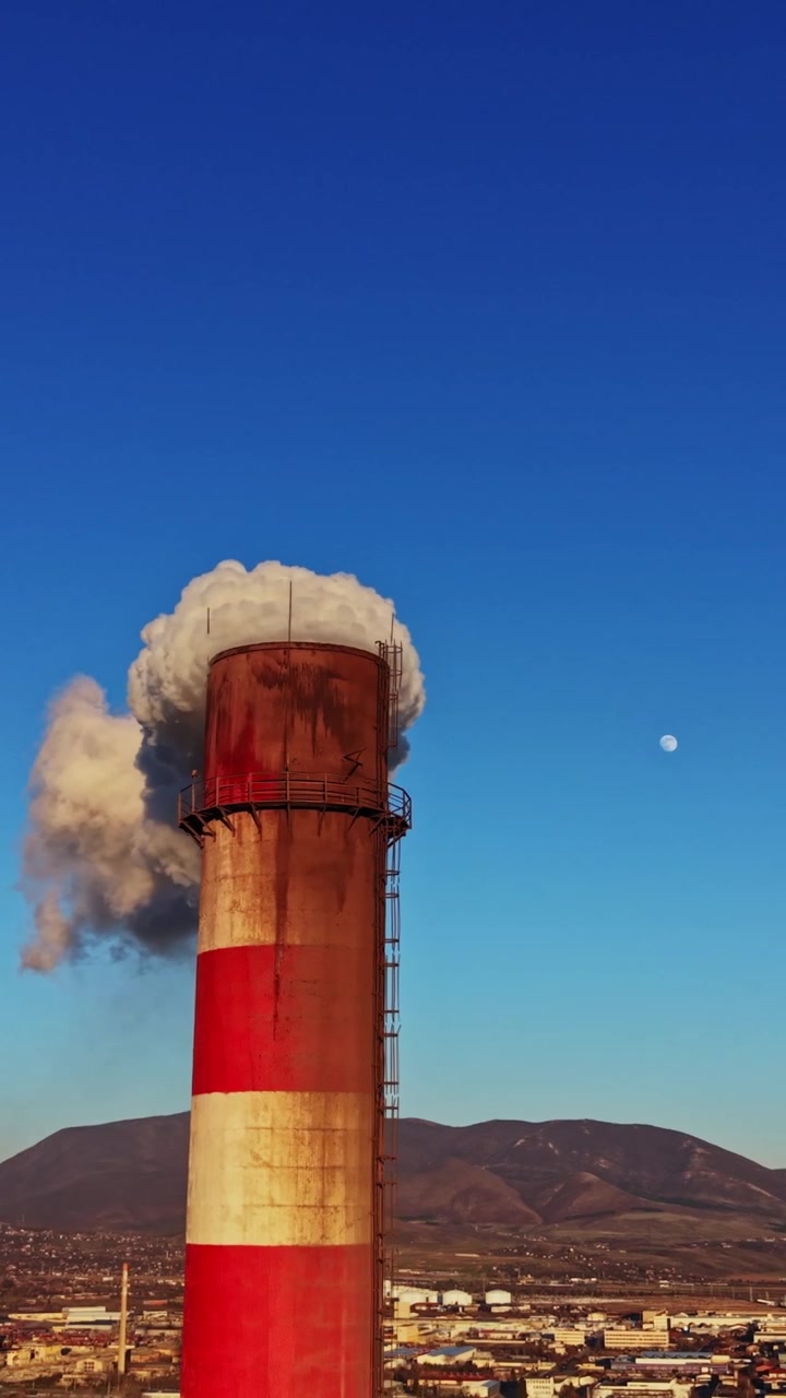 Il camino di una fabbrica rilascia fumo sul paesaggio nel pomeriggio