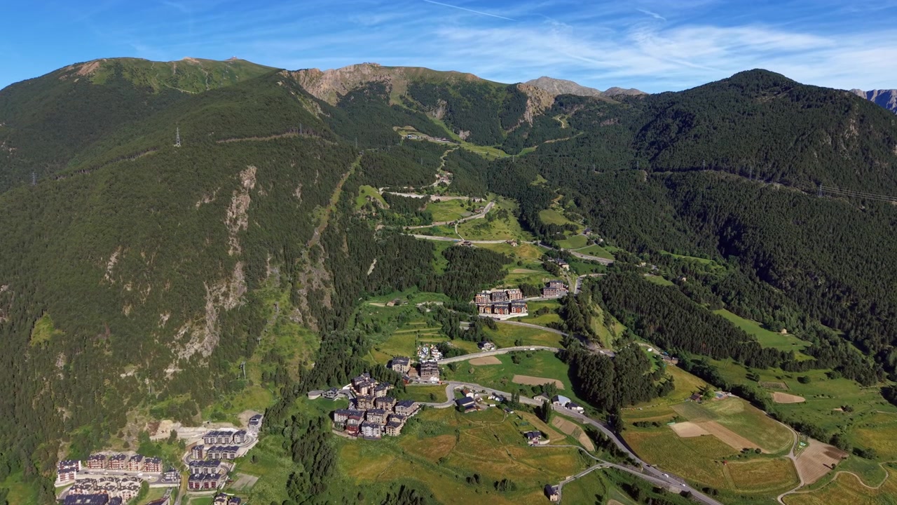 Il villaggio di Canillo immerso in una lussureggiante valle verde dei Pirenei ad Andorra, circondato da montagne boscose, strade tortuose ed edifici alpini sparsi sotto un cielo azzurro.