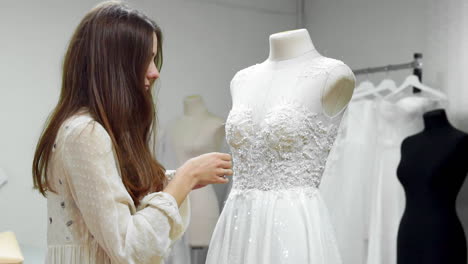 Portrait-of-a-girl-creating-a-wedding-dress-by-exclusive-order-sewing-fabrics-and-rhinestones-on-a-dress-dressed-in-a-mannequin.-production-of-wedding-dresses.-Little-business