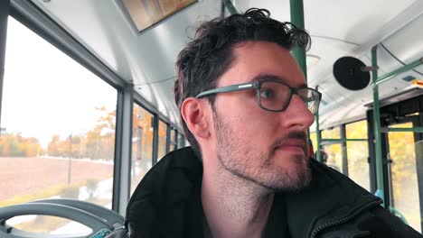 charming european man with a beard and glasses enjoys his journey as a bus passenger in germany, capturing his vibrant experience with a spontaneous selfie toward the camera