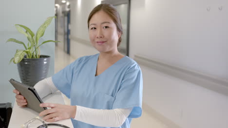 portrait of happy asian female doctor using tablet at hospital reception, copy space, slow motion