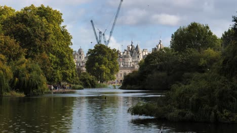 a view from st james park, royal garden near buckingham palace in westminster, london, uk. the lake surrounded by willow trees and in the background the buildings of the city.