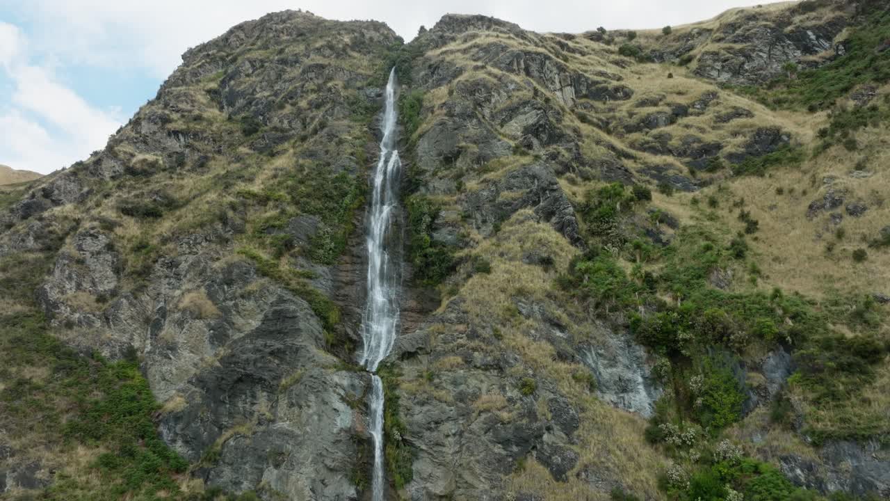 Vista aerea pittoresca di un paesaggio aspro, roccioso e montuoso con una stretta cascata che scorre liberamente nella remota natura selvaggia della Nuova Zelanda Aotearoa.