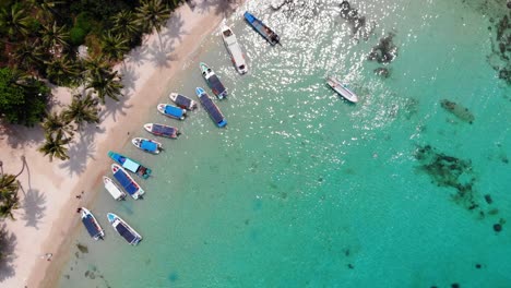 Vista-Orbital-De-Arriba-Hacia-Abajo-De-Barcos-De-Pescadores-Y-Turistas-Anclados-En-Aguas-Cristalinas-De-Color-Turquesa-Junto-A-La-Playa-De-Arena,-Isla-Del-Archipiélago-De-Vietnam,-área-De-Phu-Quoc