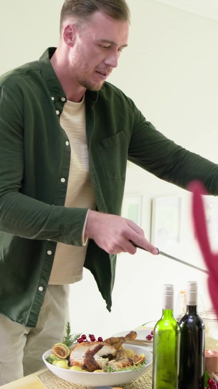 Video verticale: Solleva coltello e forchetta da intaglio, uomo in verde a casa che intaglia un arrosto, servendo la famiglia