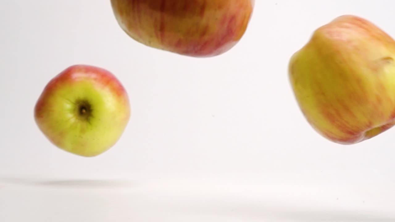 manzanas fuji rojas y amarillas enteras cayendo sobre una mesa blanca y rebotando y rodando a cámara lenta