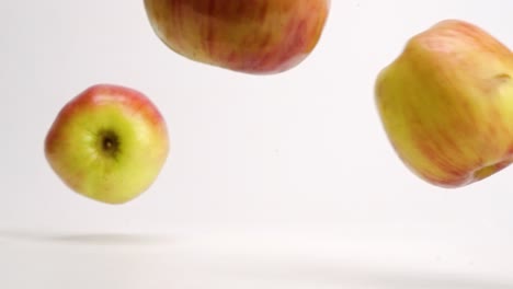 manzanas fuji rojas y amarillas enteras cayendo sobre una mesa blanca y rebotando y rodando a cámara lenta