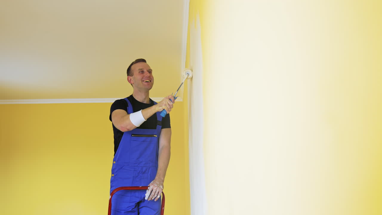 Attractive handsome repairman doing renovation the wall. Painter man at work painting an orange wall with a roller.