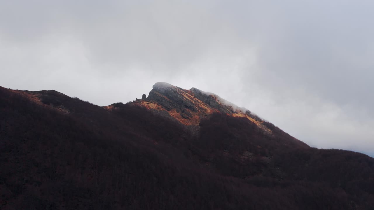 Golden sunlight hits rocky Dolomites peak through misty clouds in early autumn