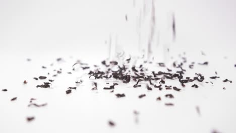 tea granules pouring down on white background - close up, slow motion