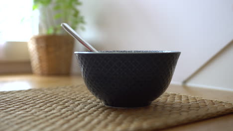 putting a blue bowl with a spoon in it on the wooden table