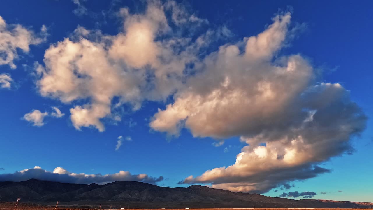 enorme cloudscape rodando sobre el desierto de mojave con coches que viajan a lo largo de la carretera en la base de las montañas - lapso de tiempo