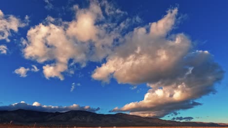 huge cloudscape rolling over the mojave desert with cars traveling along the highway at the base of the mountains - time lapse