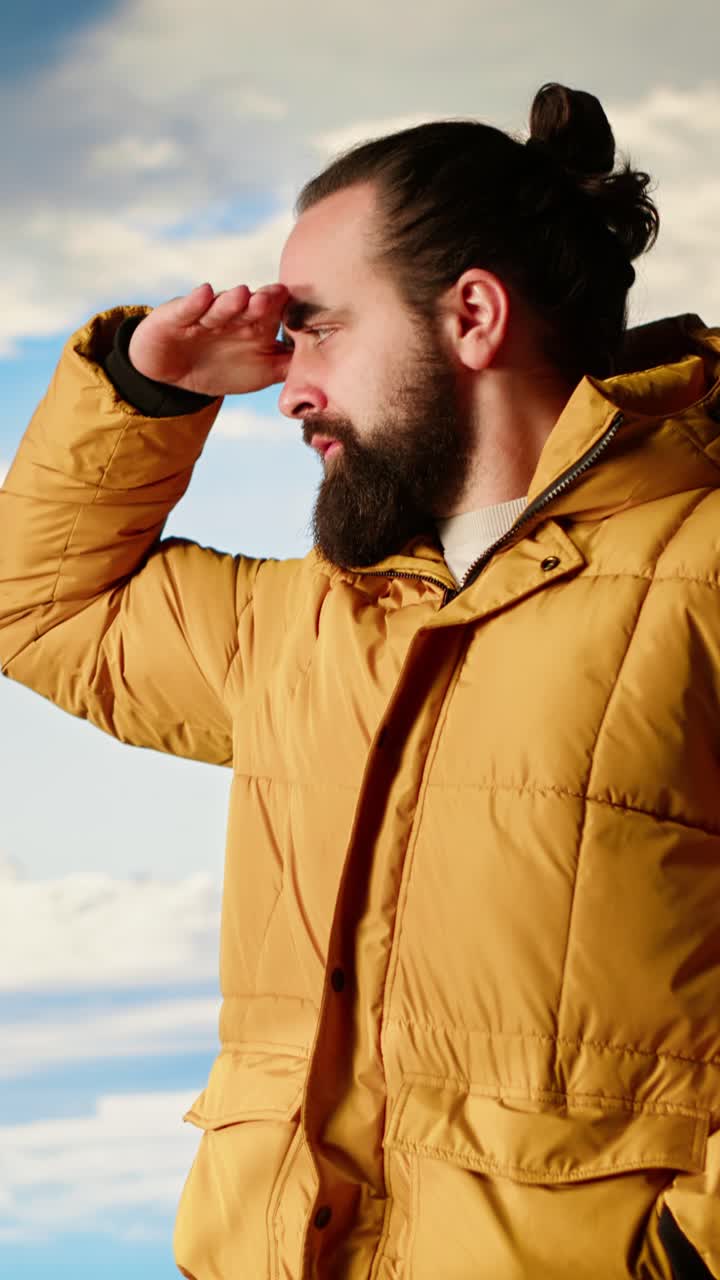 Uomo barbuto con piumino giallo che guarda in lontananza