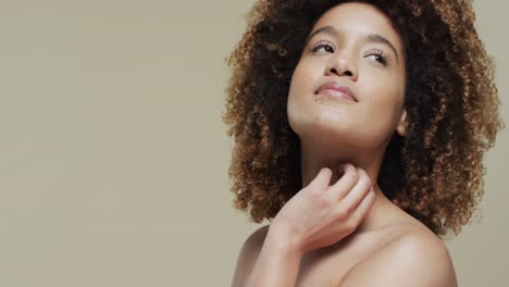 biracial woman with dark hair touching neck on beige background with copy space, slow motion