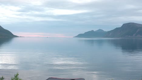 a lady standing next to a car and camping equipment beside the peaceful waters in sifjord, norway - drone flying forward