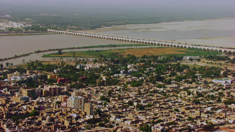 Vista-Aérea-Del-Río-Y-La-Ciudad-Con-Torres-Eléctricas-En-El-Río,-Dos-Grandes-Canales-Que-Parten-Del-Río-Y-Van-Entre-La-Ciudad,-Las-áreas-Rurales-Y-Urbanas-Reunidas-Khyberpakhtunkhwa,-Pakistán