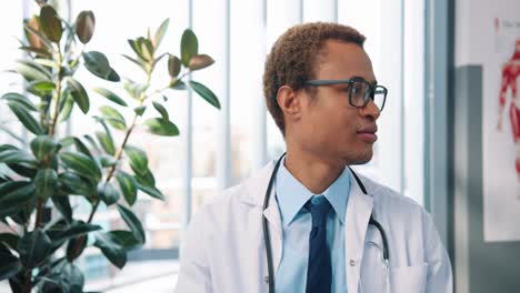 Primer-Plano-Retrato-De-Feliz-Y-Apuesto-Joven-Médico-Con-Bata-Blanca-Y-Anteojos-Mirando-La-Cámara-En-El-Gabinete-Del-Hospital-En-El-Lugar-De-Trabajo,-Hombre-Infeccioso-En-La-Clínica,-Concepto-De-Salud