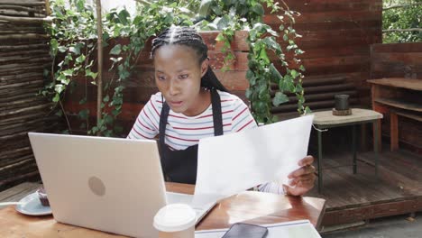 african american female coffee shop owner using laptop and doing paperwork outside, slow motion