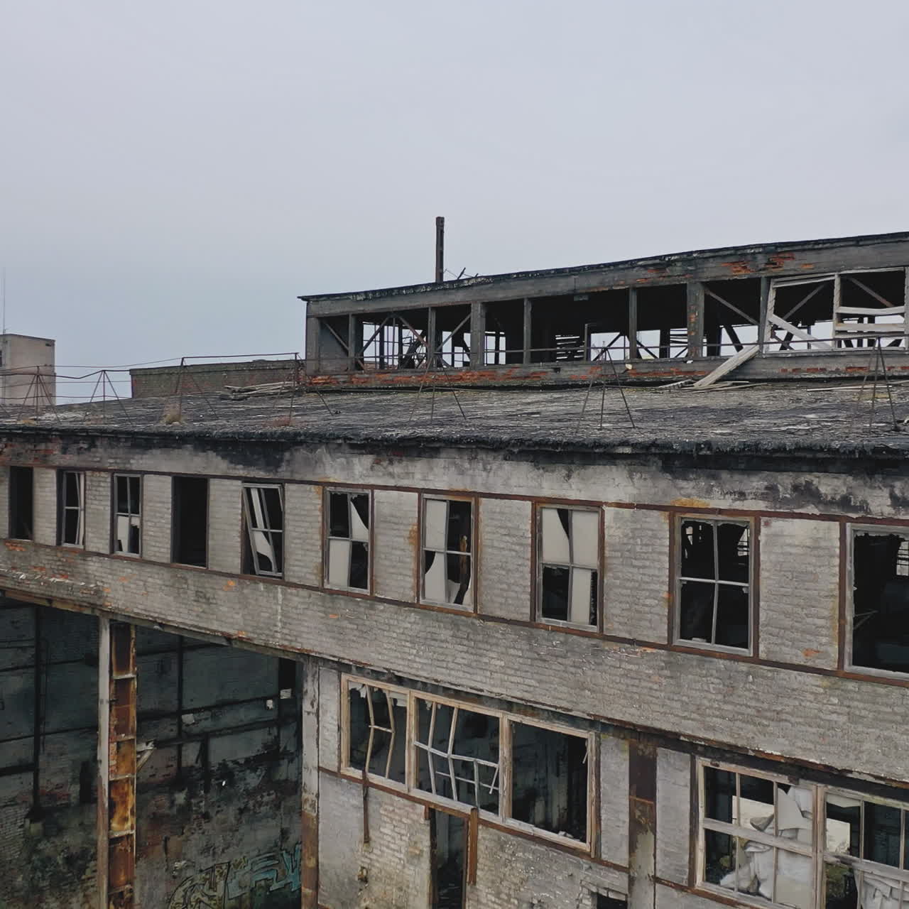 Old abandoned plant with broken windows ruined after the military actions. Demolished plant with pitted roof and some snow on the ground in winter. Aerial view