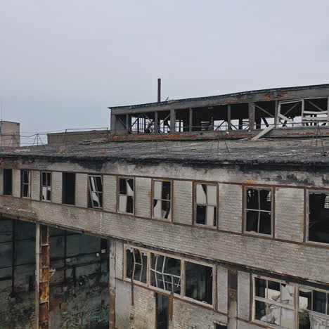 old abandoned plant with broken windows ruined after the military actions. demolished plant with pitted roof and some snow on the ground in winter. aerial view
